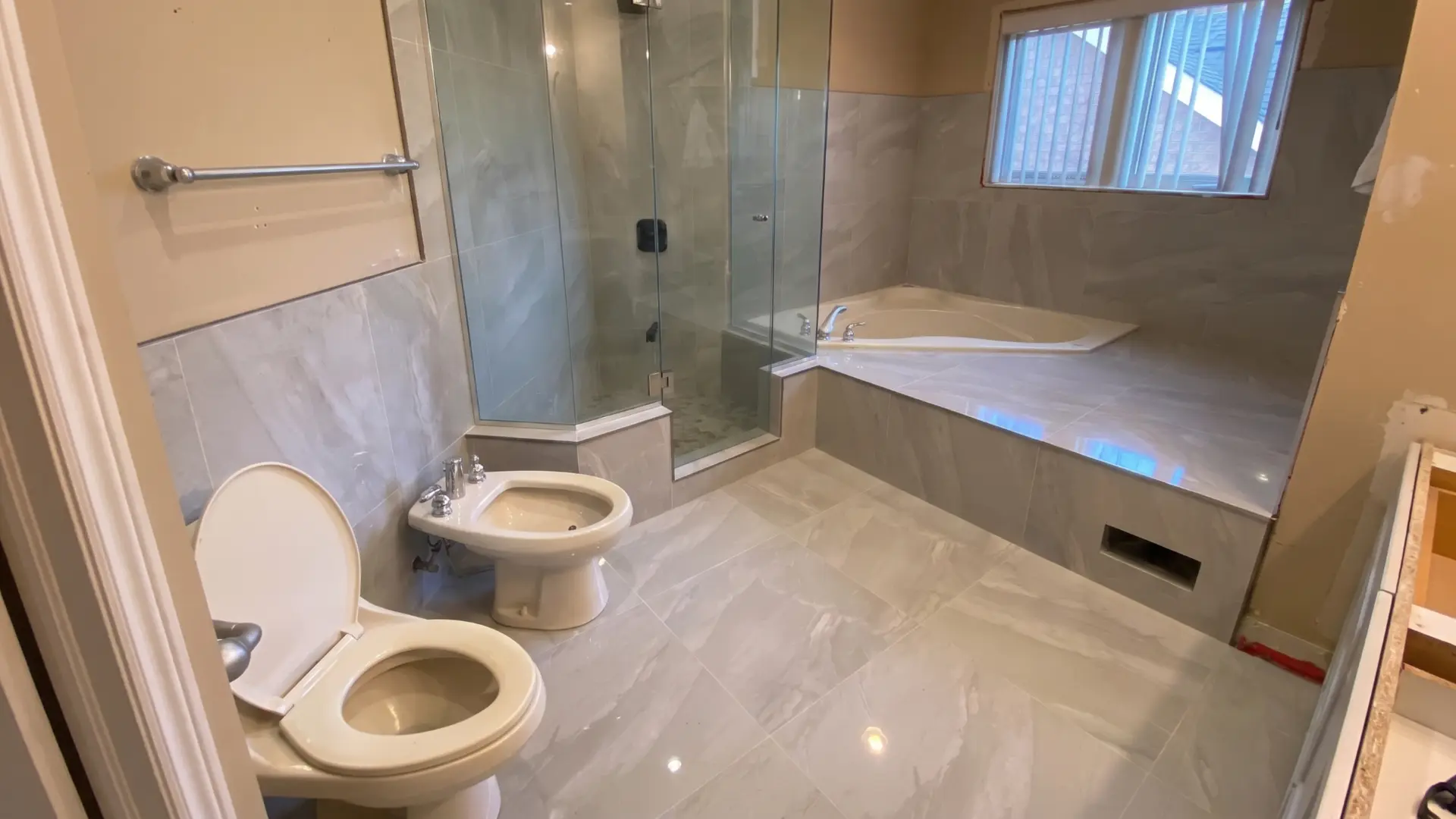 Completed bathroom with large format grey tile, glass corner shower and corner soaker tub